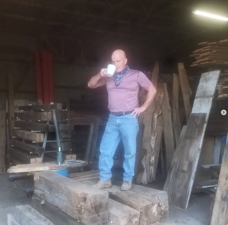 Jim standing on top of hand hewn beams while drinking a cup of coffee