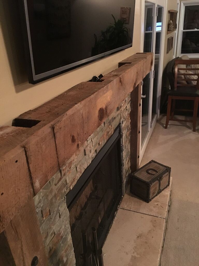 Close up of a reclaimed barn beam mantle above a stone fireplace