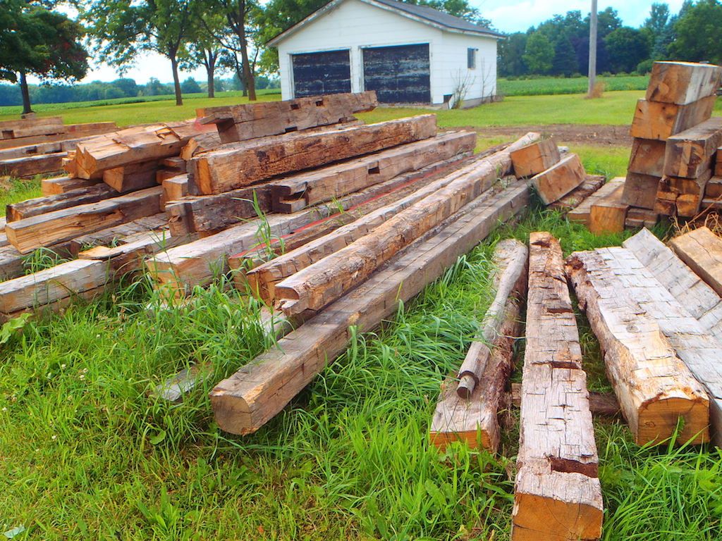 A selection of hand hewn and rough sawn barn beams laying in the grass at a demolition site